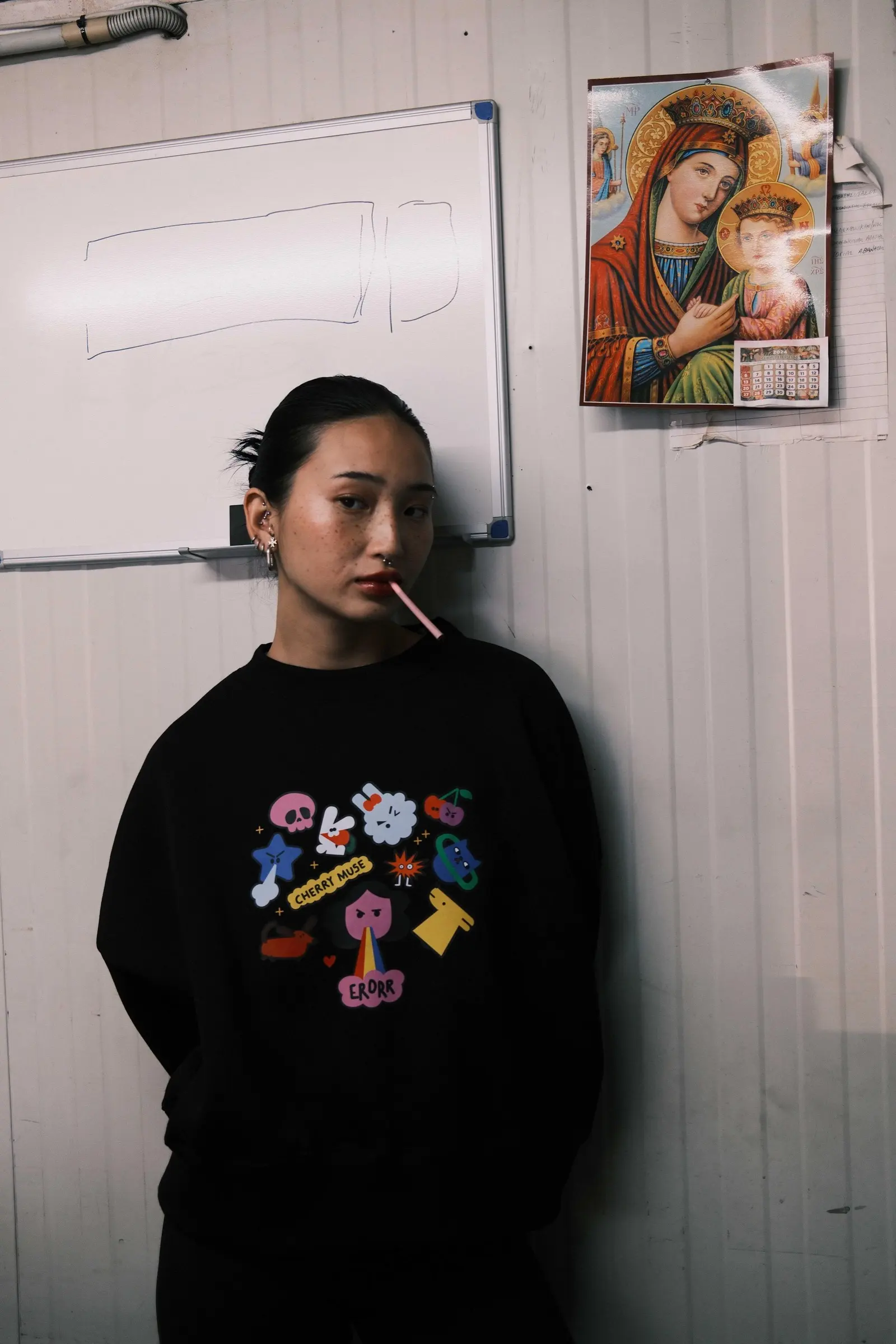 Model leaning on a wall in a black sweatshirt with a colourful doodle print