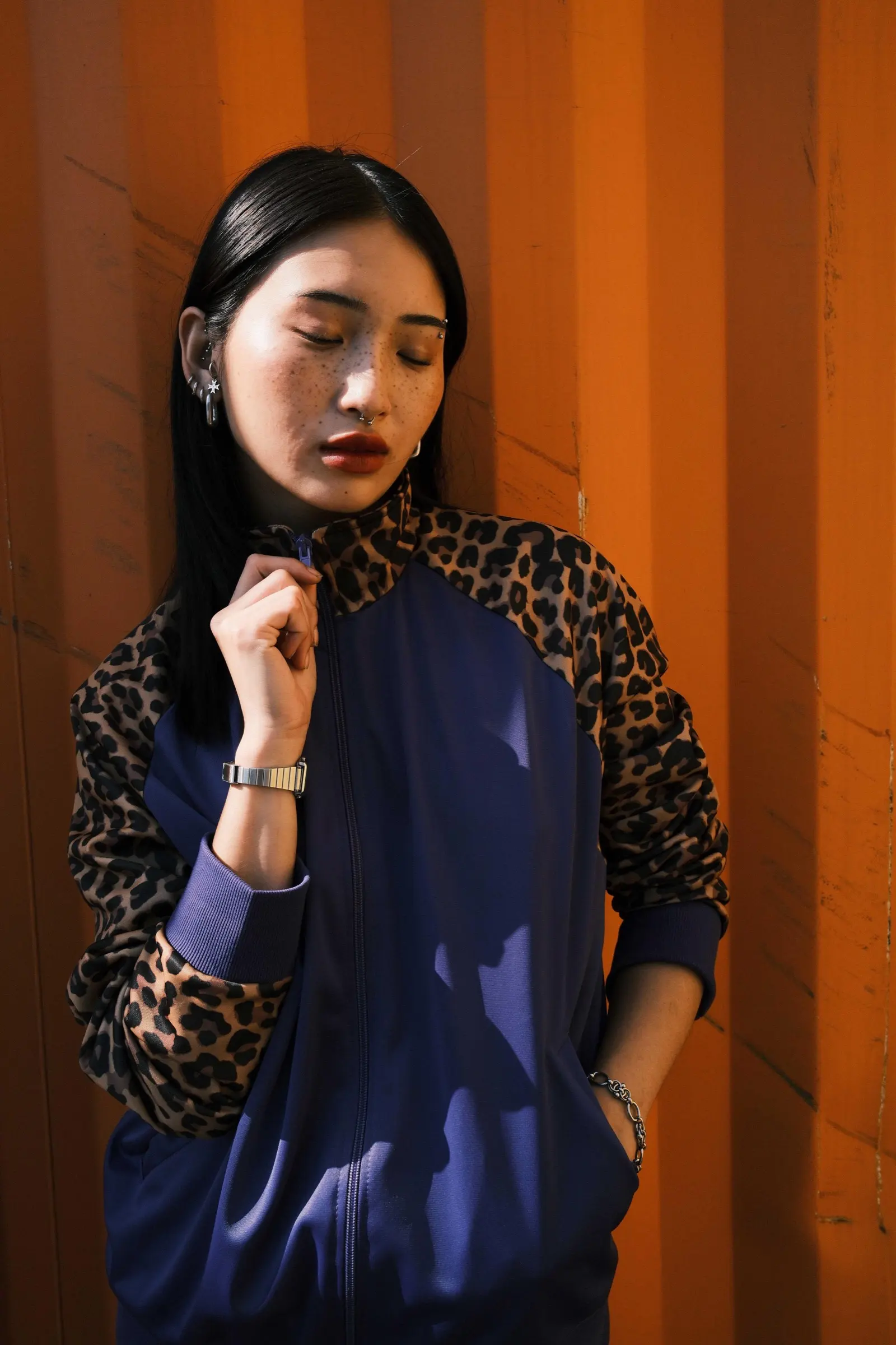 Model in a navy track jacket with leopard sleeves against an orange wall
